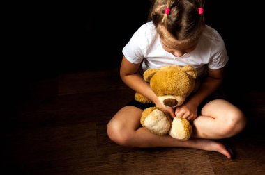 Küçük üzgün bir kız elinde oyuncakla oturuyor. Çocuk yetiştirmekle ilgili sorunlar. Çocuk barınakları. Yalnız ve terk edilmiş çocuklar..