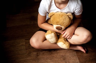 Küçük üzgün bir kız elinde oyuncakla oturuyor. Çocuk yetiştirmekle ilgili sorunlar. Çocuk barınakları. Yalnız ve terk edilmiş çocuklar..