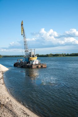 Dredger nehirde. Sahilde kum yığını. Nehrin dibini temizliyorum. Nehir akışını muhafaza et. Doğa, nehir, gökyüzü, bulutlar.
