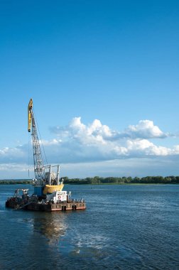 Dredger nehirde. Sahilde kum yığını. Nehrin dibini temizliyorum. Nehir akışını muhafaza et. Doğa, nehir, gökyüzü, bulutlar.