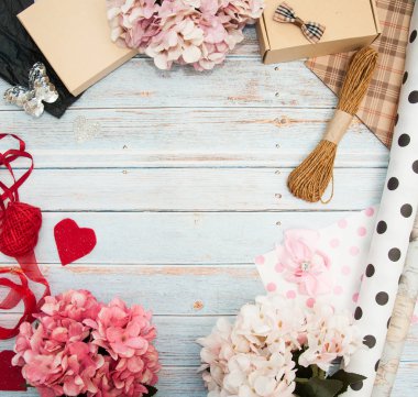 Hediye paketi. Kutular, kurdeleler, hediye kağıtları, halatlar, makas, fiyonklar, ahşap bir arka planda çiçekler. Sevgililer günü, doğum günü, anneler günü hediyeleri. Hediye paketine hazırlanılıyor.