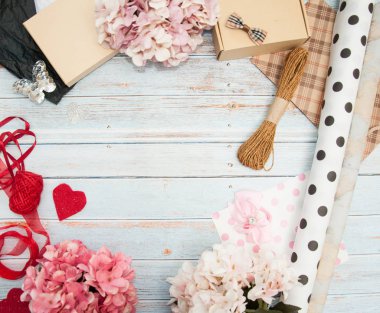 Hediye paketi. Kutular, kurdeleler, hediye kağıtları, halatlar, makas, fiyonklar, ahşap bir arka planda çiçekler. Sevgililer günü, doğum günü, anneler günü hediyeleri. Hediye paketine hazırlanılıyor.