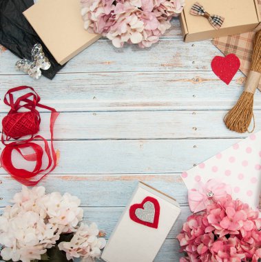 Hediye paketi. Kutular, kurdeleler, hediye kağıtları, halatlar, makas, fiyonklar, ahşap bir arka planda çiçekler. Sevgililer günü, doğum günü, anneler günü hediyeleri. Hediye paketine hazırlanılıyor.