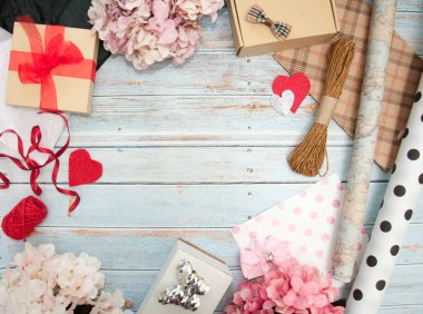 Hediye paketi. Kutular, kurdeleler, hediye kağıtları, halatlar, makas, fiyonklar, ahşap bir arka planda çiçekler. Sevgililer günü, doğum günü, anneler günü hediyeleri. Hediye paketine hazırlanılıyor.