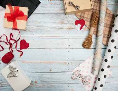 Hediye paketi. Kutular, kurdeleler, hediye kağıtları, halatlar, makas, fiyonklar, ahşap bir arka planda çiçekler. Sevgililer günü, doğum günü, anneler günü hediyeleri. Hediye paketine hazırlanılıyor.