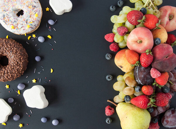 Много натуральных и здоровых витаминов фрукты, ягоды против сладкой и нездоровой пищи на черном фоне. Веганская экологически безопасная еда. Правильные продукты для потери веса и неправильные продукты для набора веса. Выбор:
