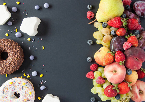 Много натуральных и здоровых витаминов фрукты, ягоды против сладкой и нездоровой пищи на черном фоне. Веганская экологически безопасная еда. Правильные продукты для потери веса и неправильные продукты для набора веса. Выбор:
