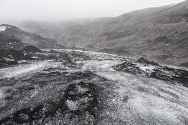 İzlanda'daki Solheimajokull kül gösterilen buzul buzu ve kayalıklarla ve arka planda küçük bir şelale üzerinde kazık.