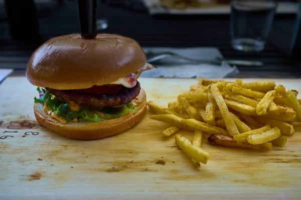 Lekker eten hamburger en frietjes op een oude houten plaat. — Stockfoto