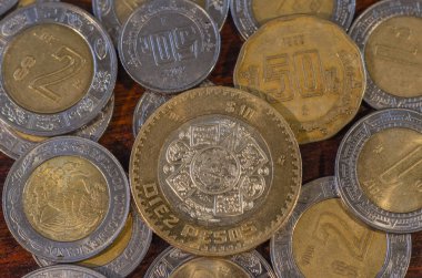 Mexican Coin in the middle of other coins in a table of wood suggesting good economy clipart