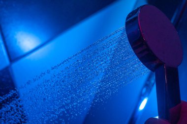 Kız, duş kabininde mavi arka lambalı bir su bidonu tutuyor. Bir su bidonundan düşen su damlaları.