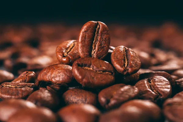 Grains of black coffee on a black granite countertop with yellow light from behind. Advertising photo of coffee. Pour coffee. Macro photo of grains.