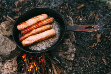 Kızartma tavasında açık ateşte kızarmış sosis. Doğada yemek hazırlıyorum. Açık havada öğle yemeği. Ormanda piknik. Yemek yanıyor.