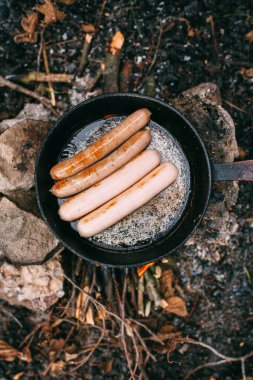Kızartma tavasında açık ateşte kızarmış sosis. Doğada yemek hazırlıyorum. Açık havada öğle yemeği. Ormanda piknik. Yemek yanıyor.