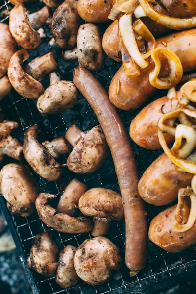 Cooking sausages with onions, mushrooms on the grill. Cooking on charcoal. Food on the nature. Lunch at the campsite. Picnic. Photo is close