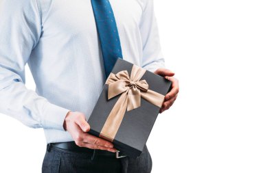 Bir adam elinde kahverengi bir kurdeleyle bir hediye tutuyor. Beyaz arka planda açık tişörtlü, kravatlı bir adam. Ellerinde siyah hediye kutusu.