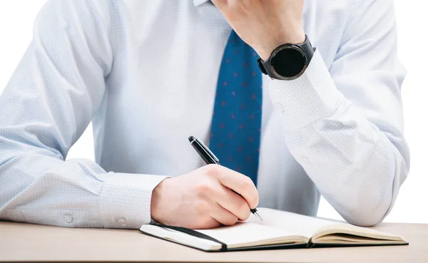 A business man writes with a pen in a black notebook while sitting at a table.The guy holds on to his head. Smart watch on a hand.