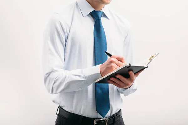 The guy writes in a black notebook. A man on a white background with a blue tie in a white shirt. Note in the notebook.