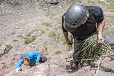 One man climber working  with the rope after putting up the route climbed in order to secure the second climber on a climbing wall inside central Andes mountains at Santiago, Chile clipart