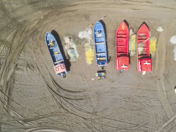 An aerial view directly above of the fishing boats over the sand while a crane try to pull from the sand to the sea the cute fishing boats. Amazing fishery at Chile with all the boats in a row line
