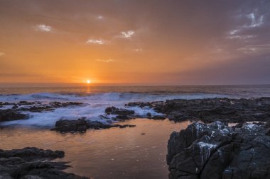Anzota Mağaraları 'nda güneş batıyor. Güneş ışınları bulutları aydınlatıyor ve Pasifik Okyanusu suları üzerinde inanılmaz yansımalarla dalgalar kayaların üzerinde hareket ederken.