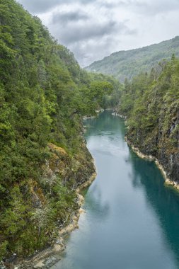 Kuzey Şili Patagonya 'daki dehşet verici köprü, Puelo nehri, dramatik bir gökyüzü altında engebeli engebeli doğa üzerindeki turkuvaz sularıyla dar boğazın etrafında dönüyor.