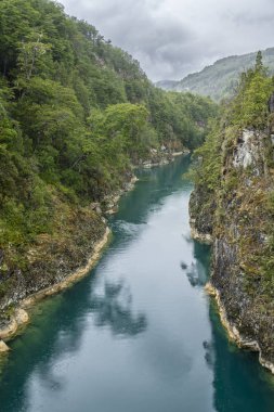 Kuzey Şili Patagonya 'daki dehşet verici köprü, Puelo nehri, dramatik bir gökyüzü altında engebeli engebeli doğa üzerindeki turkuvaz sularıyla dar boğazın etrafında dönüyor.
