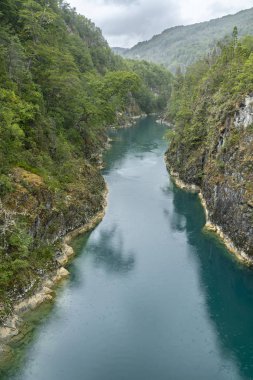 Kuzey Şili Patagonya 'daki dehşet verici köprü, Puelo nehri, dramatik bir gökyüzü altında engebeli engebeli doğa üzerindeki turkuvaz sularıyla dar boğazın etrafında dönüyor.