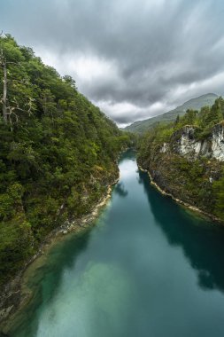 Kuzey Şili Patagonya 'daki dehşet verici köprü, Puelo nehri, dramatik bir gökyüzü altında engebeli engebeli doğa üzerindeki turkuvaz sularıyla dar boğazın etrafında dönüyor.