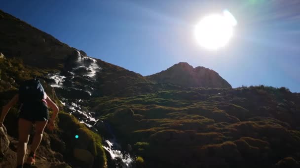 アンデス山脈の中の滝を横断する2人の女性ハイカーが 太陽のシルエットを背後にしています アンデス渓谷の風景で巨大な険しい地形の素晴らしい眺め ハイキングのための畏敬のしい旅行先 — ストック動画
