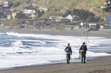 Güneşli bir günde kumsalda yürüyen balıkçılar.