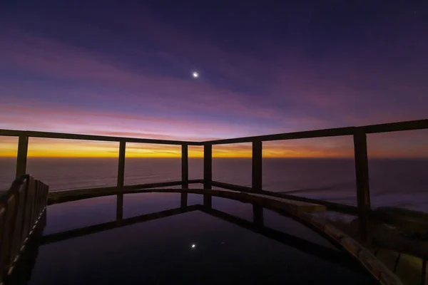 An amazing an idyllic view a wooden hot tub waiting us for some relaxation time during sunset and twilight before an awe night sky with a small crescent moon. A leisure activity at Chilean coastline