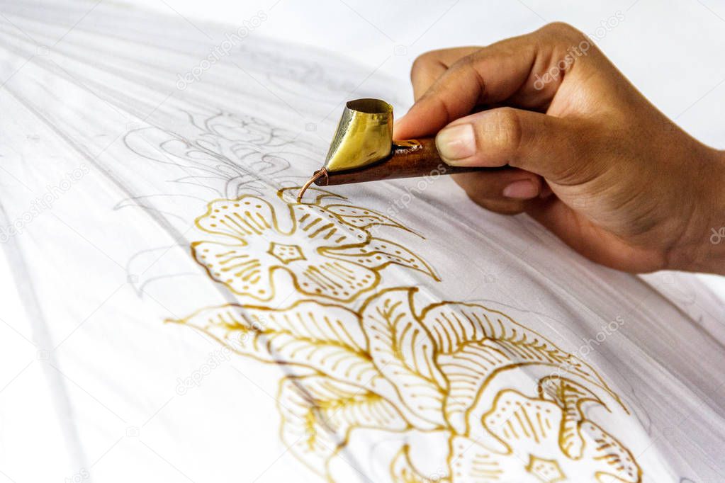 Isolated hand in the process of making Indonesian batik with floral pattern