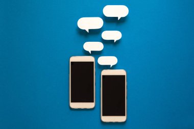 Kağıt konuşma balonları üzerinde mavi arka plan ile akıllı telefonlar. İletişim kavramı. Üstten Görünüm. Uzay kopyalayın. Kağıt kompozisyon