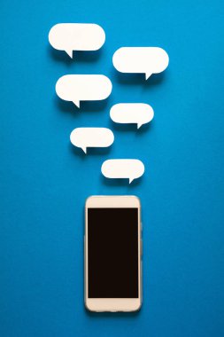 Kağıt konuşma balonları üzerinde mavi arka plan ile akıllı telefonlar. İletişim kavramı. Üstten Görünüm. Uzay kopyalayın. Kağıt kompozisyon