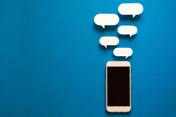 Kağıt konuşma balonları üzerinde mavi arka plan ile akıllı telefonlar. İletişim kavramı. Üstten Görünüm. Uzay kopyalayın. Kağıt kompozisyon