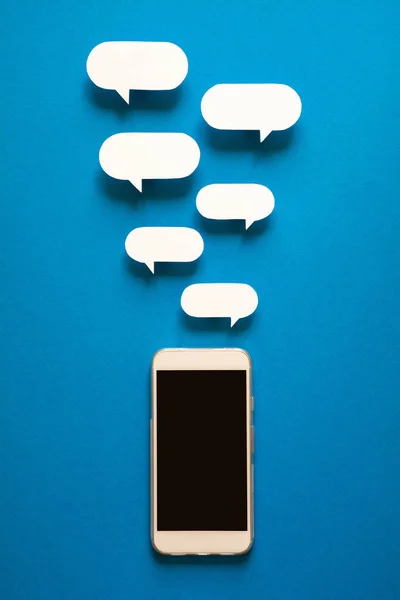 Kağıt konuşma balonları üzerinde mavi arka plan ile akıllı telefonlar. İletişim kavramı. Üstten Görünüm. Uzay kopyalayın. Kağıt kompozisyon