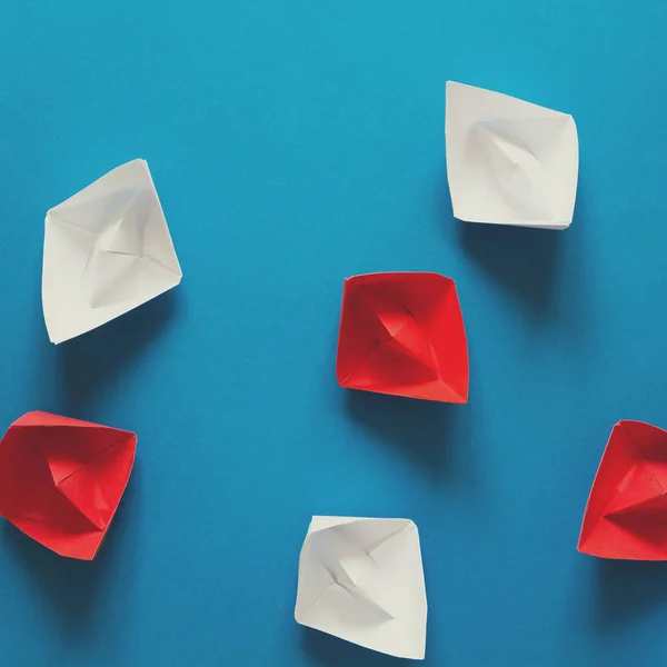 Set of red and white origami boats on blue paper background. Summer traveling concept. Top view. Toned