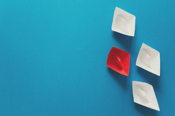 Set of red and white origami boats on blue paper background. Summer traveling concept. Top view. Toned