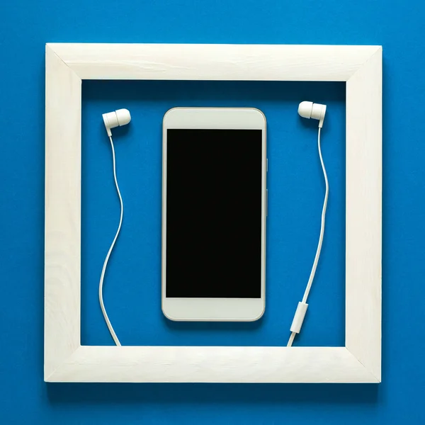 Minimalism. Masterpiece in wooden frame. Smartphone with headphones. Top view. Flat lay. Technology as art concept.