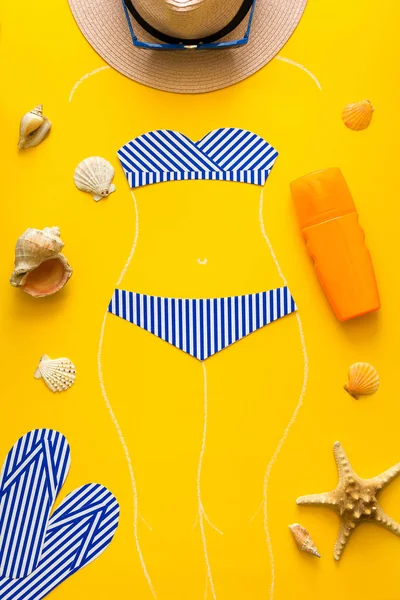 Outlines of girl in paper swimsuit drowing by chalk. Beach accessories. Top view. Flat lay. Summer travel and sun protection concept. Origami. Mock-up