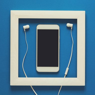 Minimalizm. Ahşap çerçeve şaheser. Kulaklıklar ile Smartphone. Üstten görünüm. Düz yatıyordu. Teknoloji Sanat kavram olarak. Tonda