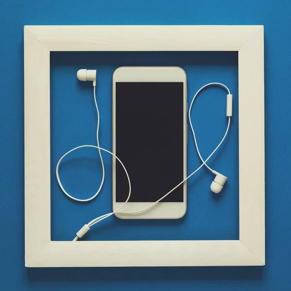 Minimalism. Masterpiece in wooden frame. Smartphone with headphones. Top view. Flat lay. Technology as art concept. Toned