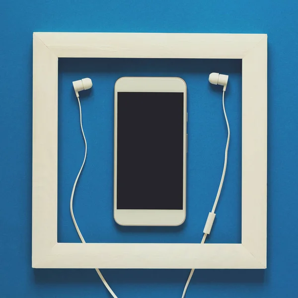 Minimalism. Masterpiece in wooden frame. Smartphone with headphones. Top view. Flat lay. Technology as art concept. Toned