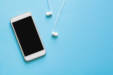 Üstten görünüm mock-up akıllı telefon ve kulaklık mavi zemin üzerine. Düz yatıyordu. Kopya için alan