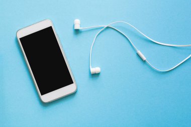 Üstten görünüm mock-up akıllı telefon ve kulaklık mavi zemin üzerine. Düz yatıyordu. Kopya için alan