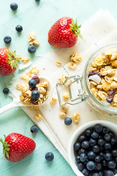 Hindistan cevizi cips, Kuruyemiş ve turkuaz ahşap zemin üzerine kuru yaban mersini ile ev yapımı granola cam kavanoz. Olgun çilek ve böğürtlen. Üstten görünüm. Düz yatıyordu. Kopya alanı