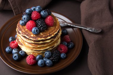 Taze yaban mersini, ahududu ve böğürtlen kahverengi plaka üzerinde krep yığını