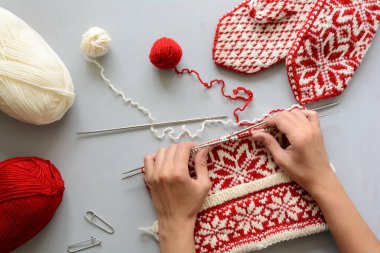 Kız şapka örgü iğneleri gri ahşap arka plan üzerinde kırmızı ve beyaz jacquaed dokuma kumaşlar. Örgü işlemi. Üstten görünüm. Düz yatıyordu