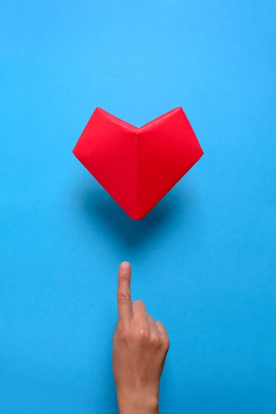 Heart health or Valentine\'s day concept. Hand indicating on red paper heart. Origami. Paper cut style.